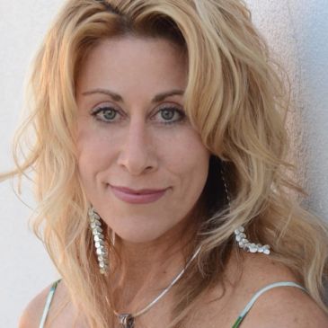 Smiling woman with wavy blonde hair and dangling earrings.