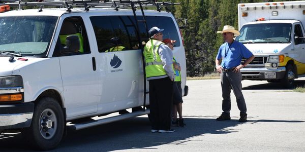 Two men and a child talking near white service vans in a sunny outdoor setting.