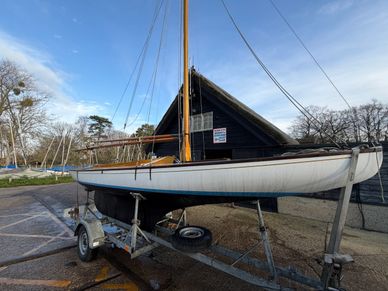 A classic sailboat on a trailer at a yacht club on a clear day.