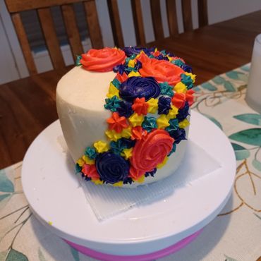 Small cake decorated with colorful frosting flowers on a white stand.