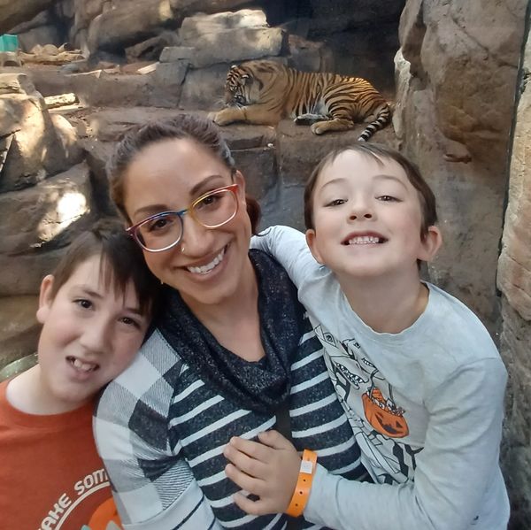 A happy family poses in front of a resting tiger at an indoor zoo exhibit.