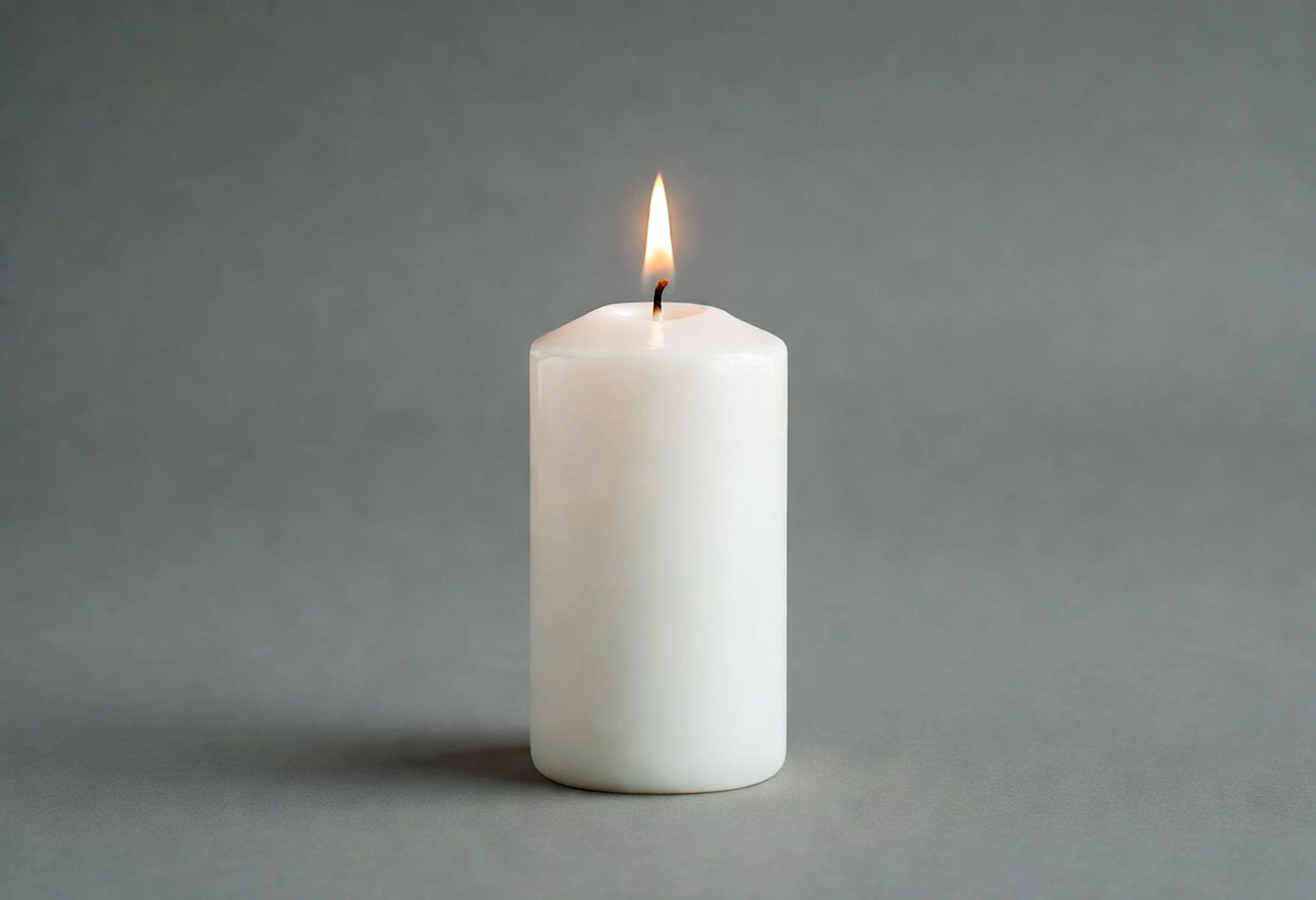 A white candle burning against a gray background.
