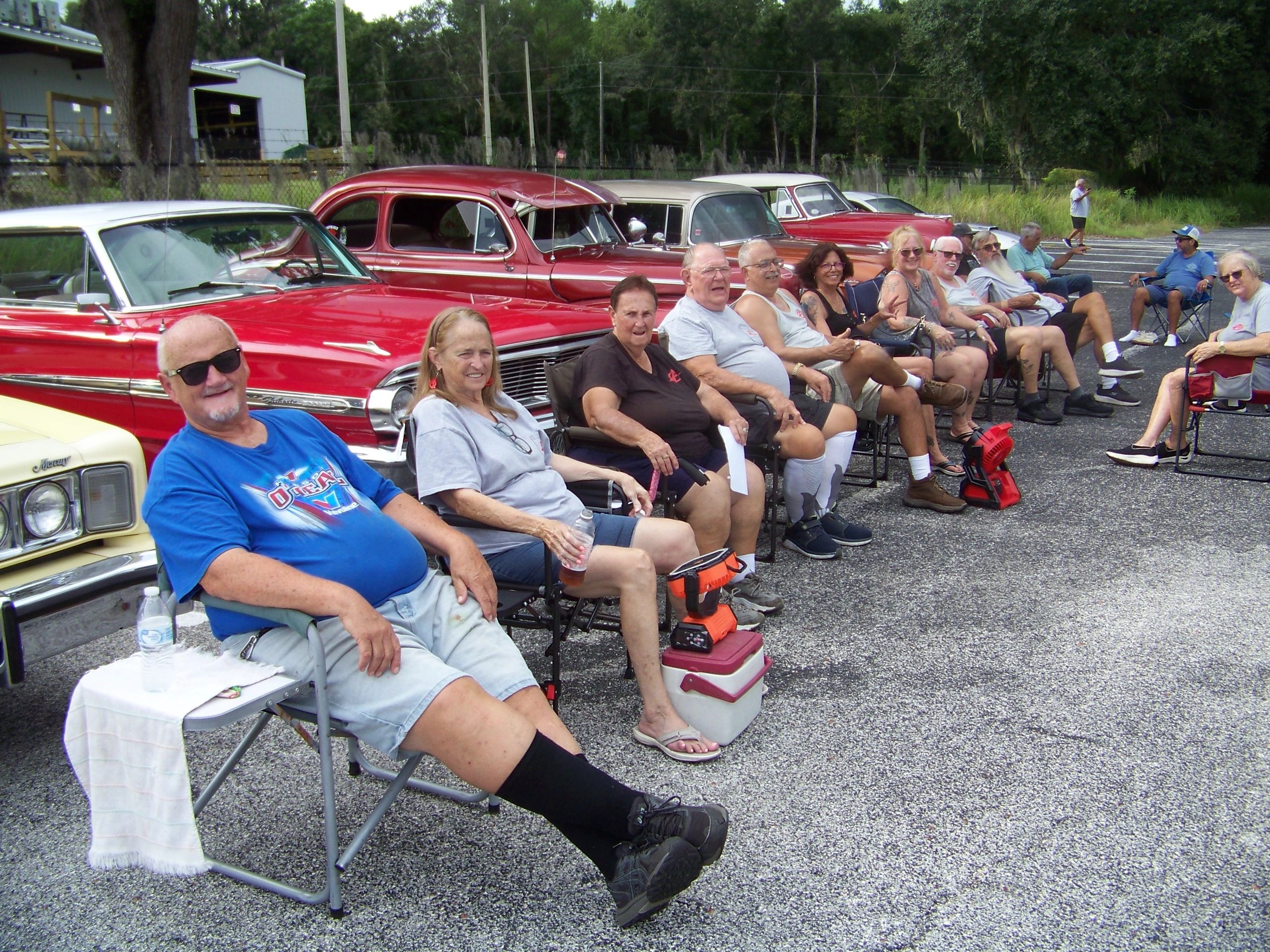 Group of people sitting in front of classic cars.