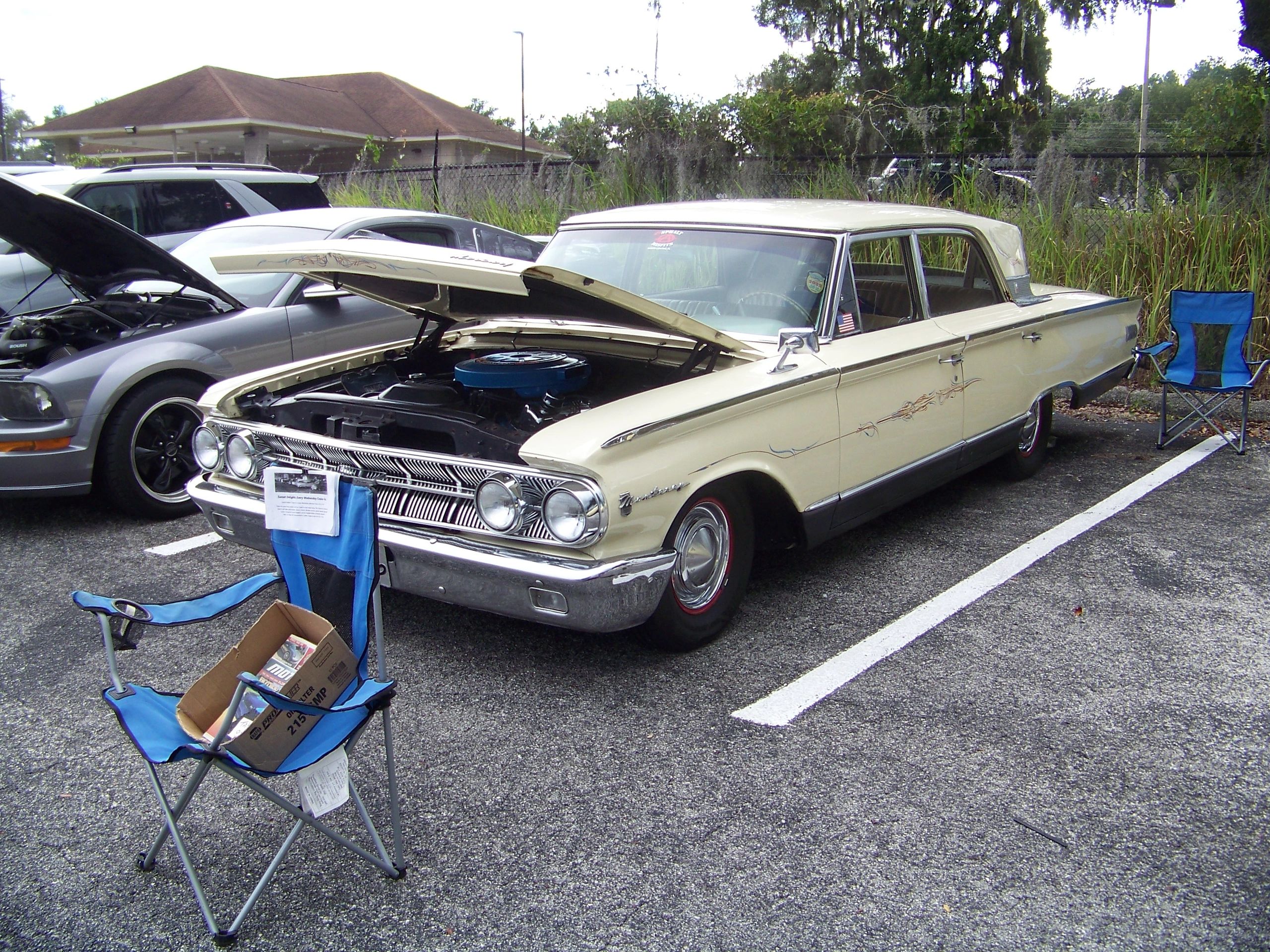 Classic cream-colored Mercury car with hood open at a car show.