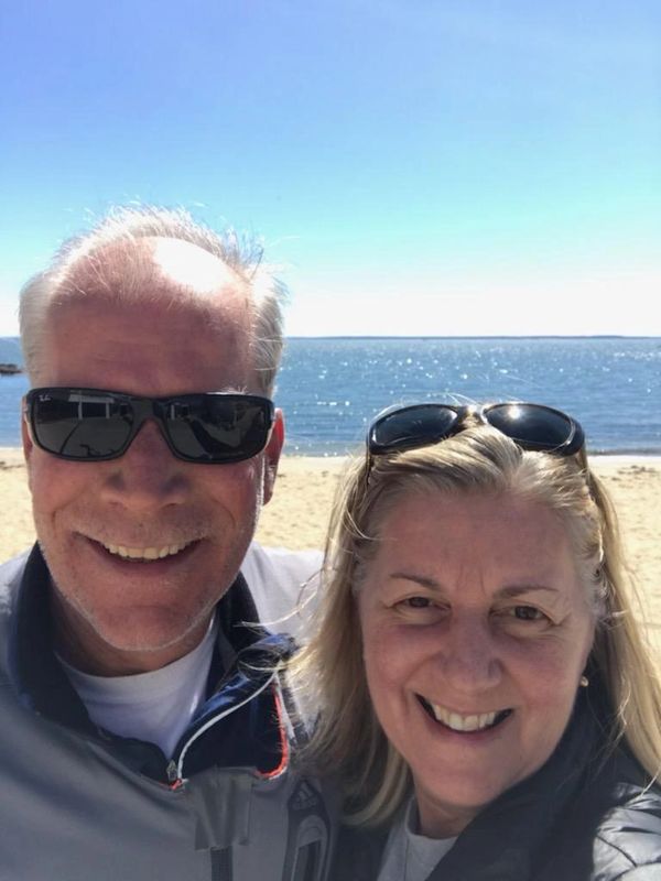 Smiling couple wearing sunglasses at the beach on a sunny day.