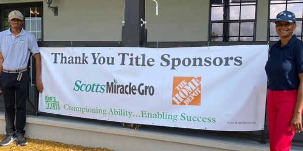 Two people stand beside a banner thanking title sponsors Scotts Miracle-Gro and The Home Depot.