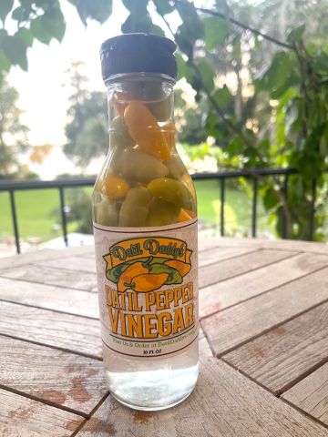 Bottle of Datil Pepper Vinegar on a wooden table outdoors.