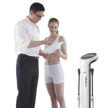 A man explains body analysis results to a woman next to a body composition machine.