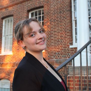 Young woman smiling outdoors against a brick building.