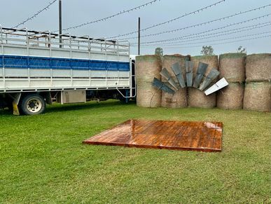 Wooden platform on grass with hay bales and a truck in the background.