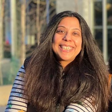 Smiling woman with long dark hair enjoying sunlight outdoors.