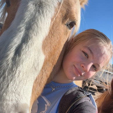 A girl taking a close-up selfie with a horse under clear blue sky.
