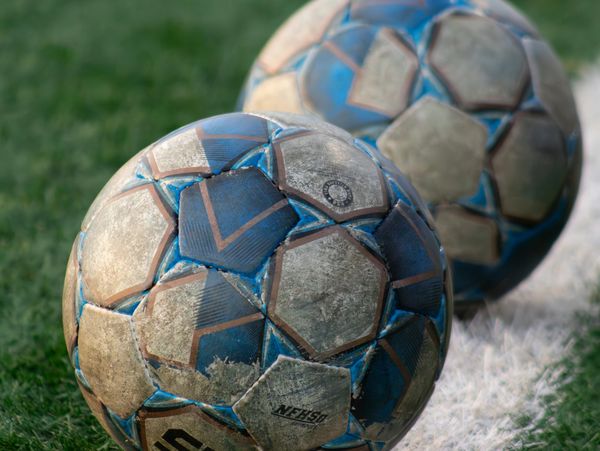 Two worn blue and white soccer balls on a grass field near a white line.