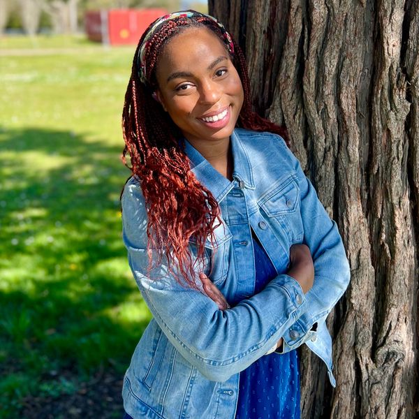 Smiling woman in denim jacket leaning on tree.