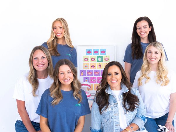 A group of six smiling women posing against a white background.