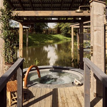 Cozy outdoor hot tub overlooking a serene river under a wooden pergola.