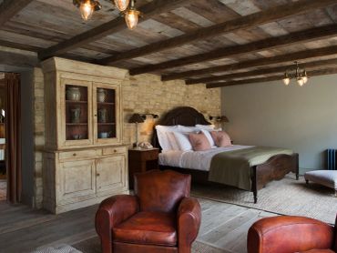 Rustic bedroom with wooden beams, leather chairs, and cozy bedding.