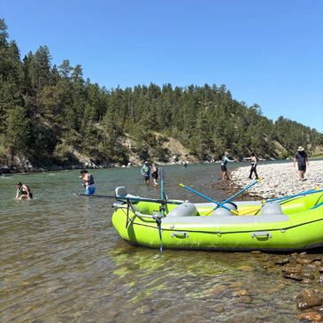 People enjoying a river day with a green inflatable raft on the shore.
