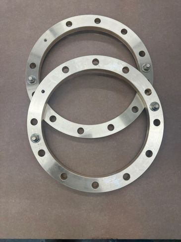 Two metal circular flanges with bolt holes and bolts on a flat surface.