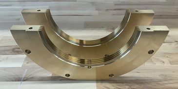 Two semi-circular brass components with holes, placed on a wooden surface.