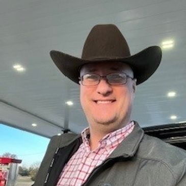 Man wearing a cowboy hat and glasses, smiling outdoors.