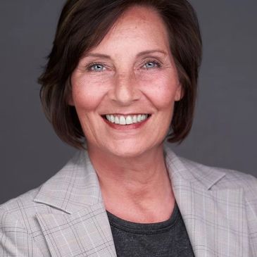 Smiling middle-aged woman with short brown hair in a gray plaid blazer.