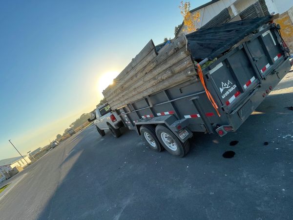 Pickup truck towing a trailer loaded with wooden logs at sunset.