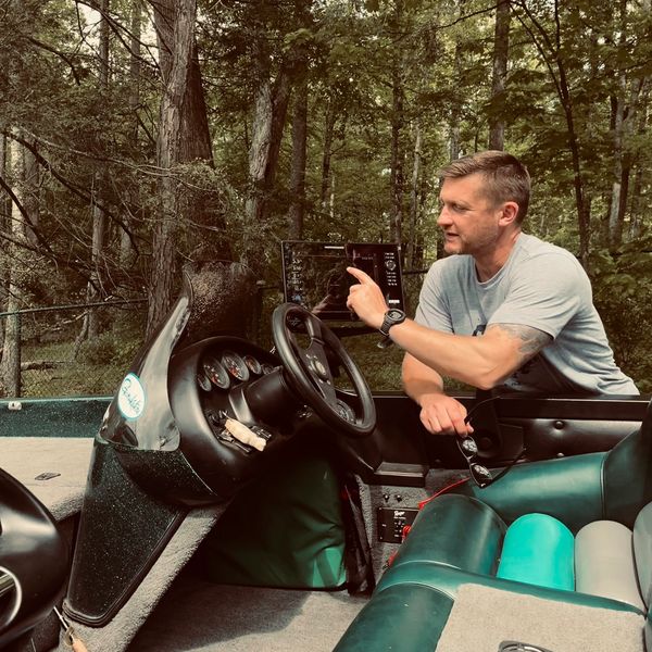 Man interacting with a touchscreen device on a boat in a wooded area.