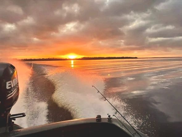 Boat cruising on calm water at sunset with fishing rods visible.