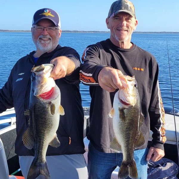 Two men proudly holding large fish on a boat under clear skies.