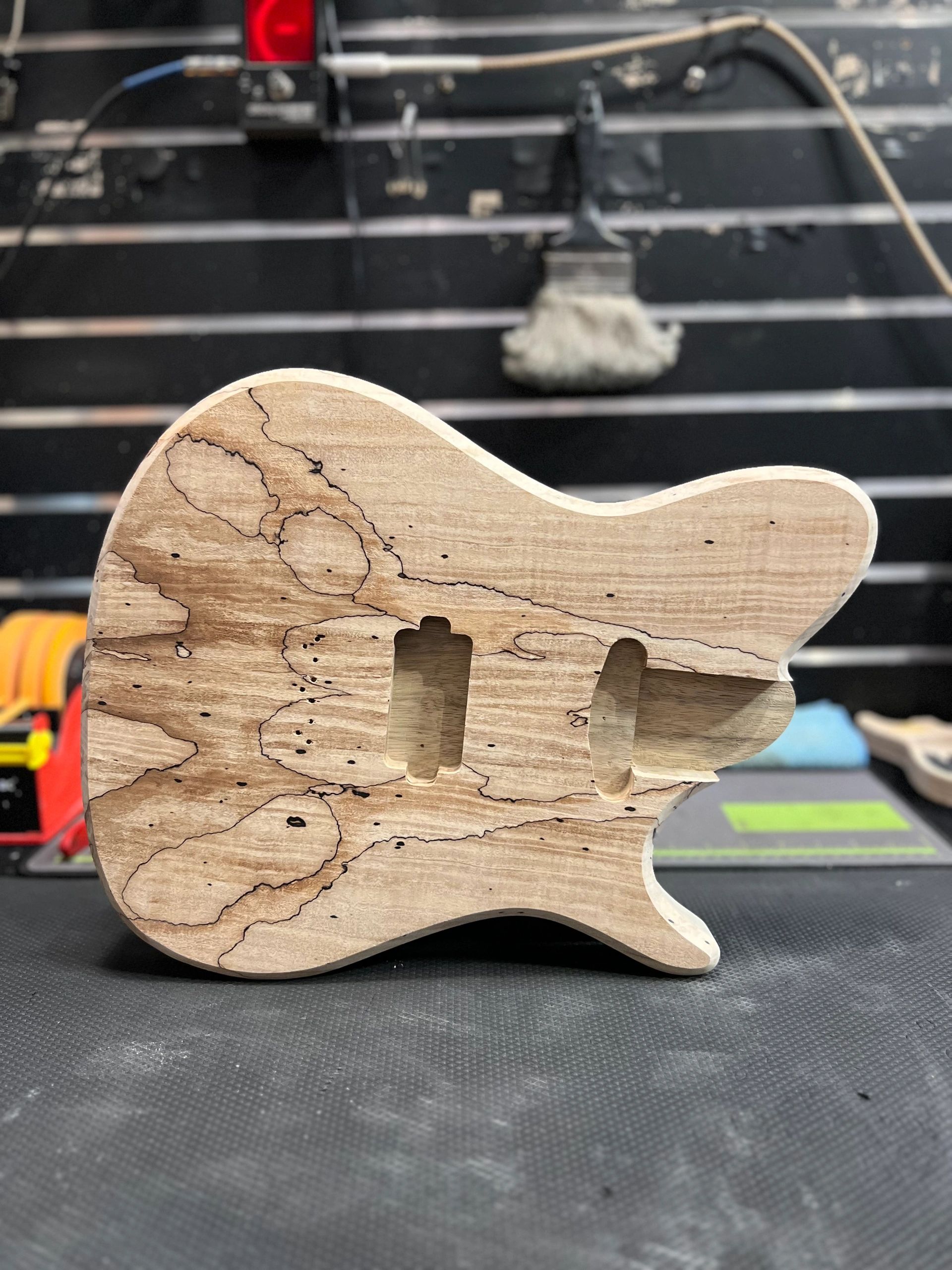 Unfinished wooden guitar body with unique grain patterns on a black surface.