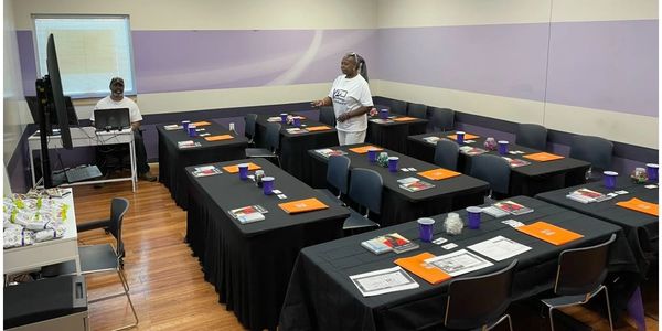 Classroom setup with tables, chairs, and two people.