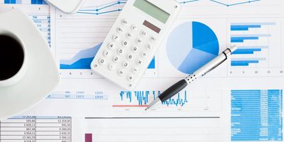 Calculator, pen, and coffee cup on financial charts and graphs.