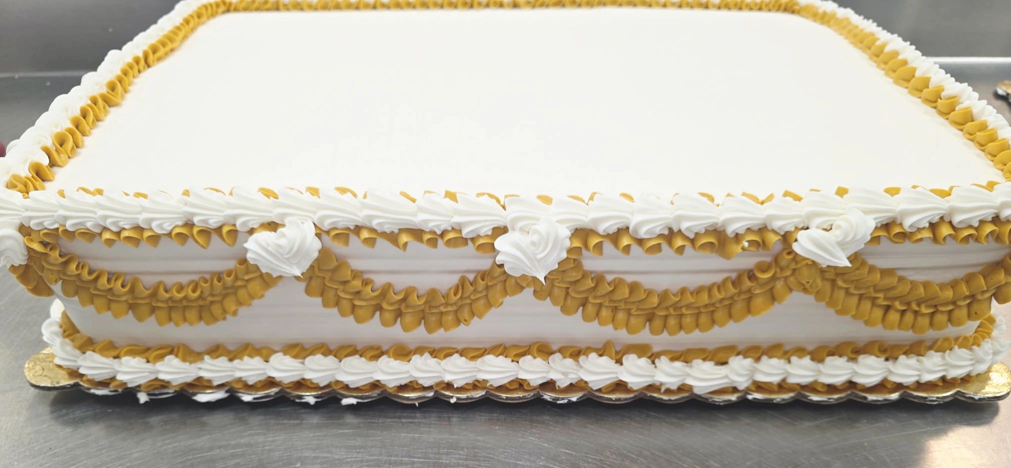 Rectangular cake with white and gold frosting decorations, ready for customization.