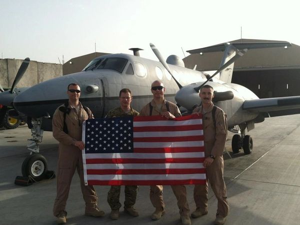 Post-mission crew holding flag in front of MC-12W in Afghanistan.