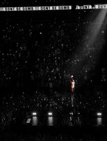 Performer illuminated on stage with crowd and 'DON'T BE DUMB' signs overhead.