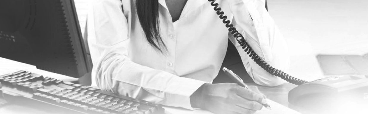 Professional woman on phone taking notes at office desk with computer.