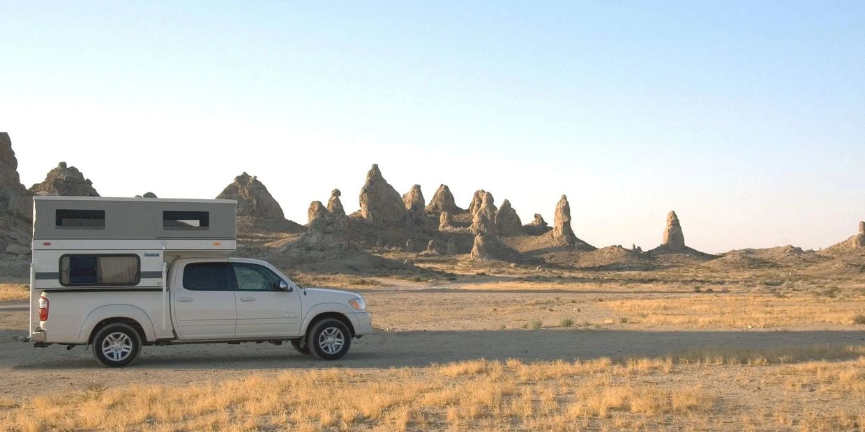 Pickup truck with camper parked in a desert with rocky formations at sunset.