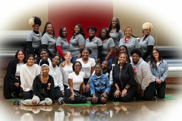 Group photo of smiling women and girls indoors, some in matching gray shirts.