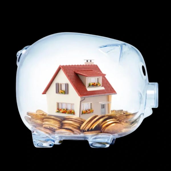 A house model inside a transparent piggy bank filled with coins.