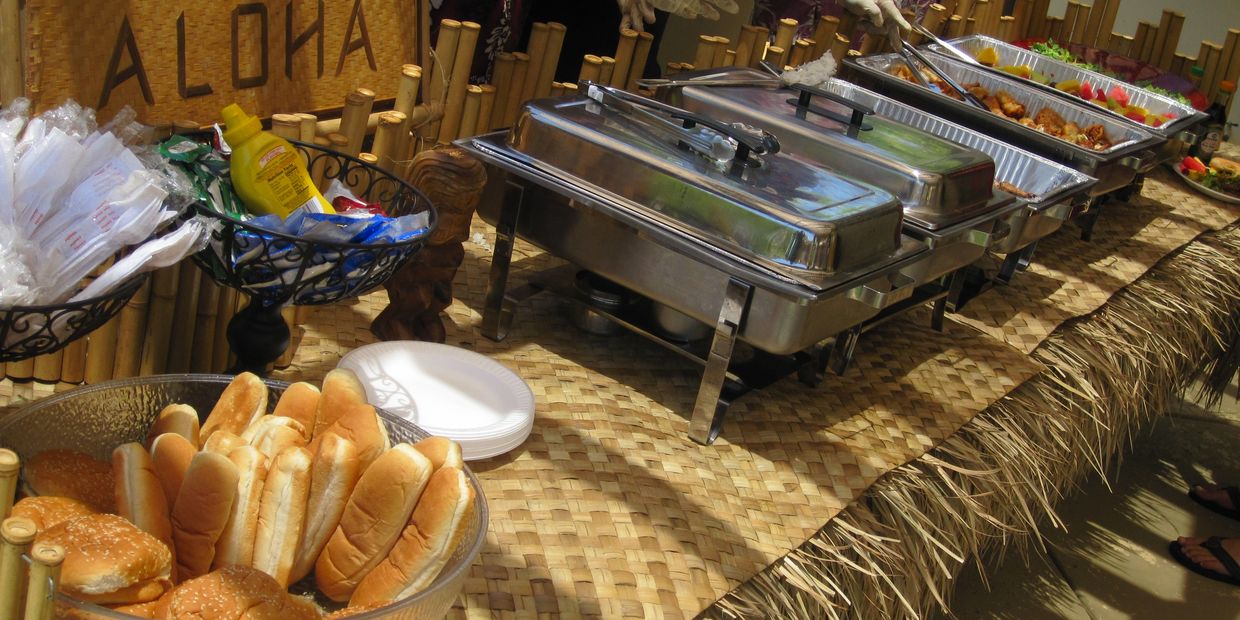 Aloha-themed buffet with rolls, condiments, and chafing dishes.