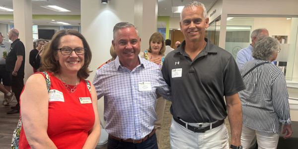 Three smiling adults posing indoors at a social event.