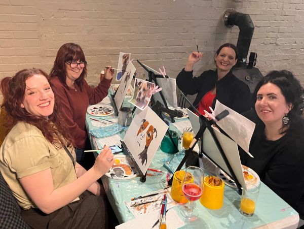 Four women painting dog portraits together at a table.