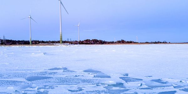 Wind turbines standing tall over a frozen, icy landscape under a clear blue sky.