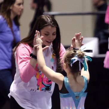 Positive and encouraging coach giving gymnast a high five.