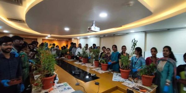 Group of people with plants in pots around a conference table.