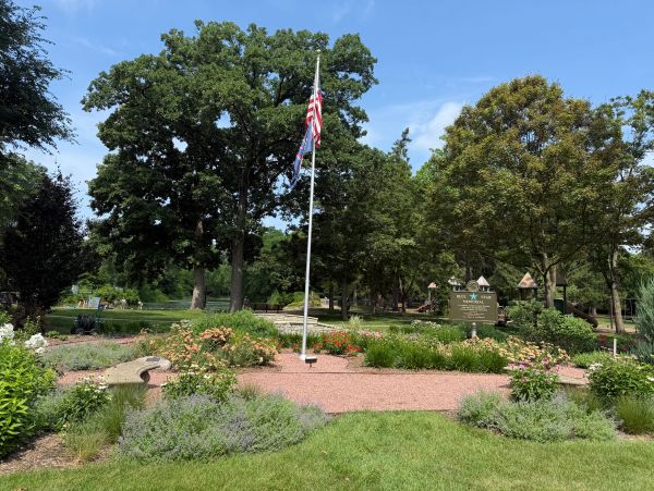 Park with flagpole and greenery under blue sky.