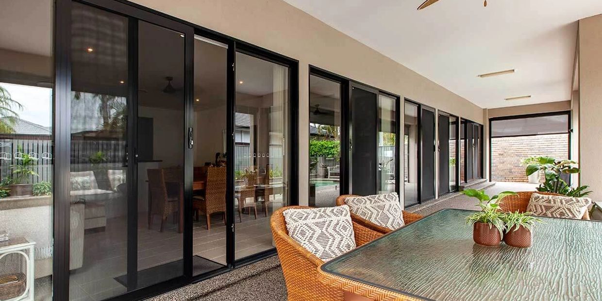 Modern outdoor patio with glass table, wicker chairs, and sliding doors.