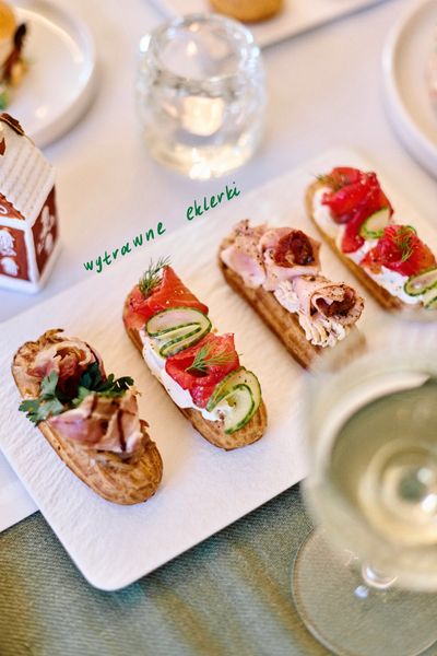 Elegant savory eclairs topped with smoked salmon, cucumber, and herbs on a white plate.