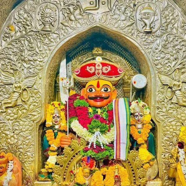 Vibrant decorated deity statue adorned with flowers and garlands in a golden ornate shrine.